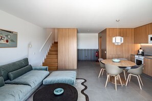 Ein modernes Wohnzimmer mit einer Couch, einem Esstisch mit Stühlen, einer Treppe und einer Küchenzeile.