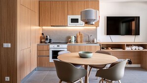 A modern kitchen with wooden cabinetry, a built-in oven, a microwave, and a dining area with a round table and chairs. - Ericeira Wave Nest by Lisbeyond (Carvoeira)