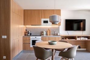 Eine moderne Küche mit Holzschränken, einem Einbauofen, einer Mikrowelle und einem Essbereich mit rundem Tisch und Stühlen.