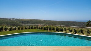 A swimming pool with a wooden deck, surrounded by a wooden fence and greenery, overlooking a hilly landscape. - Ericeira Wave Nest by Lisbeyond (Carvoeira)