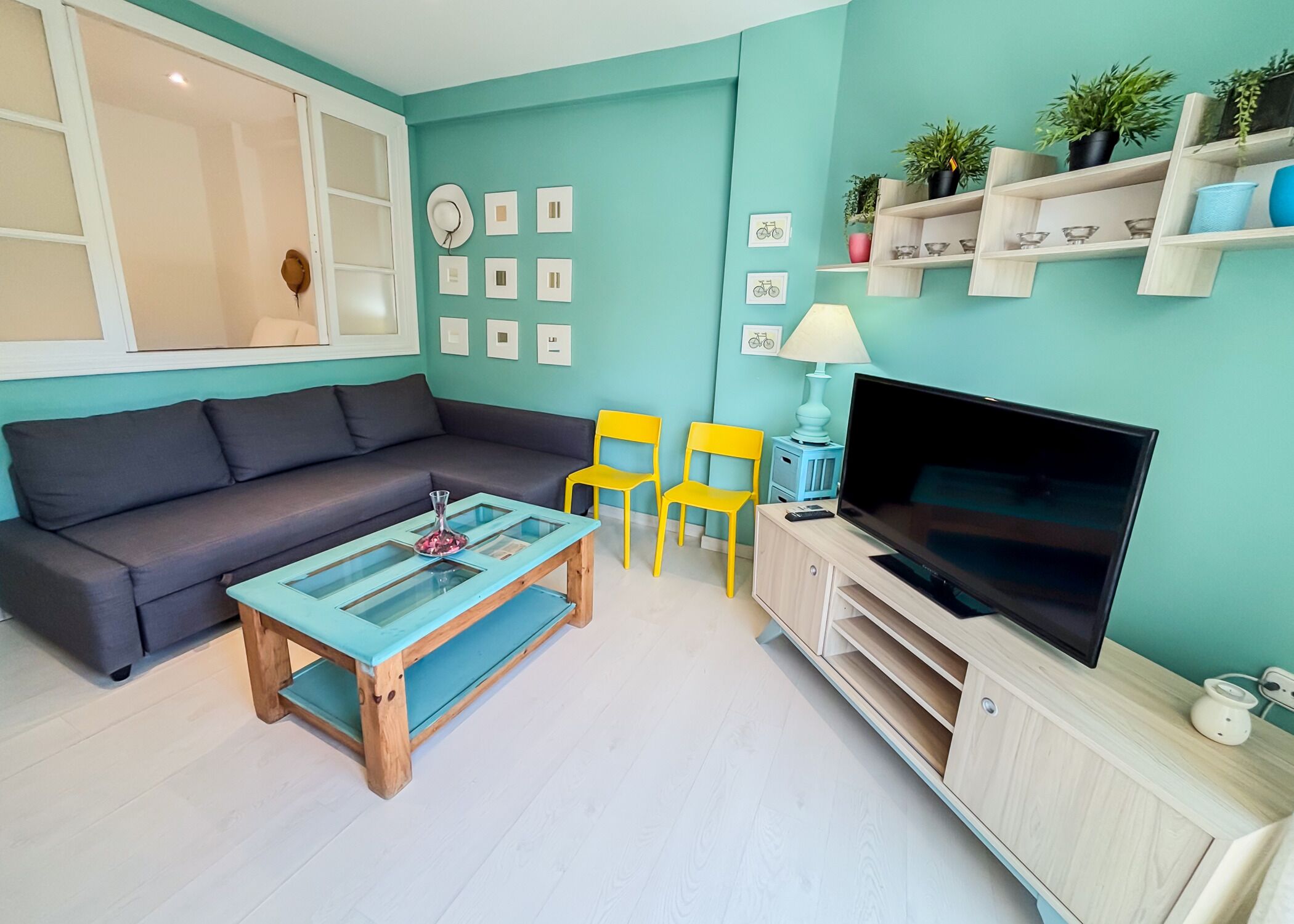 A living room with a sofa, two chairs, a coffee table, a TV, and shelves with plants.