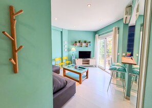 A living room with a sofa, a coffee table, a TV, and a balcony with a chair. - Skol 225 –  Beachfront studio in Marbella | Terrace & Pool (Marbella)