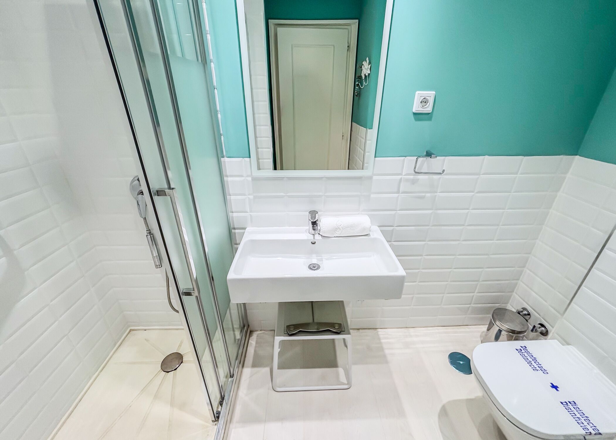 Un baño con un lavamanos blanco, un espejo, un inodoro y una cabina de ducha de vidrio.