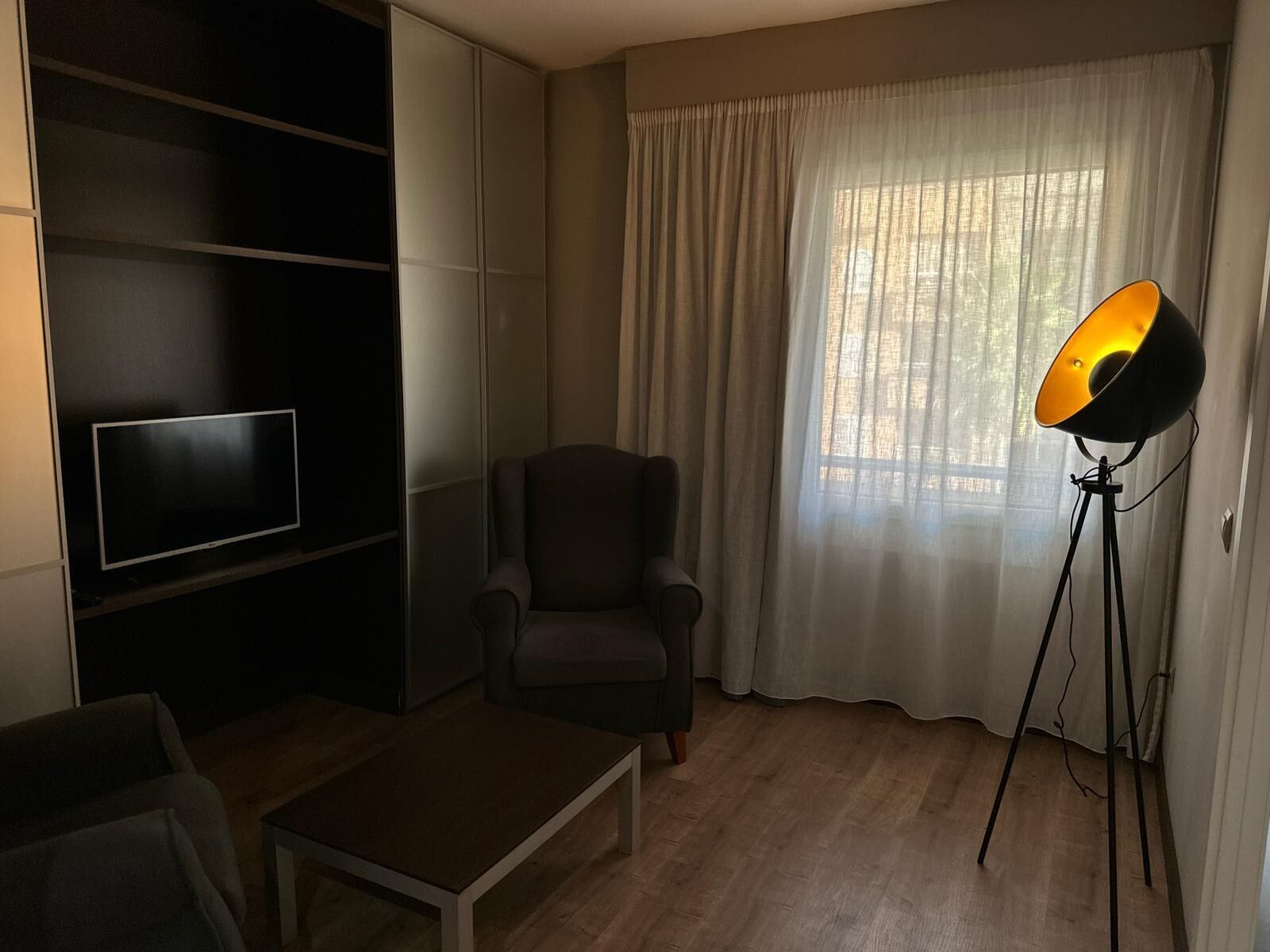 Un saló amb televisió, una cadira, una taula de centre i una làmpada de peu.