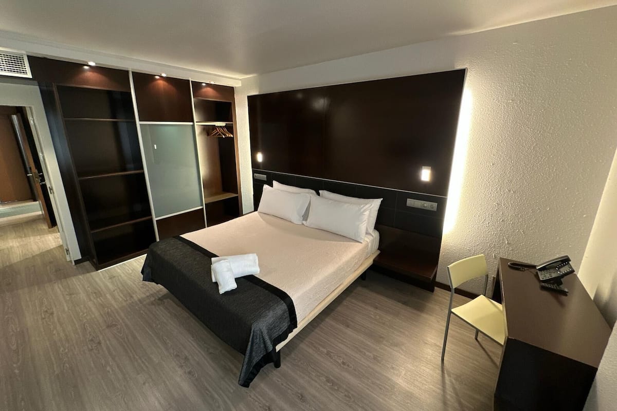A hotel room with a bed, bedside table, and a wardrobe.