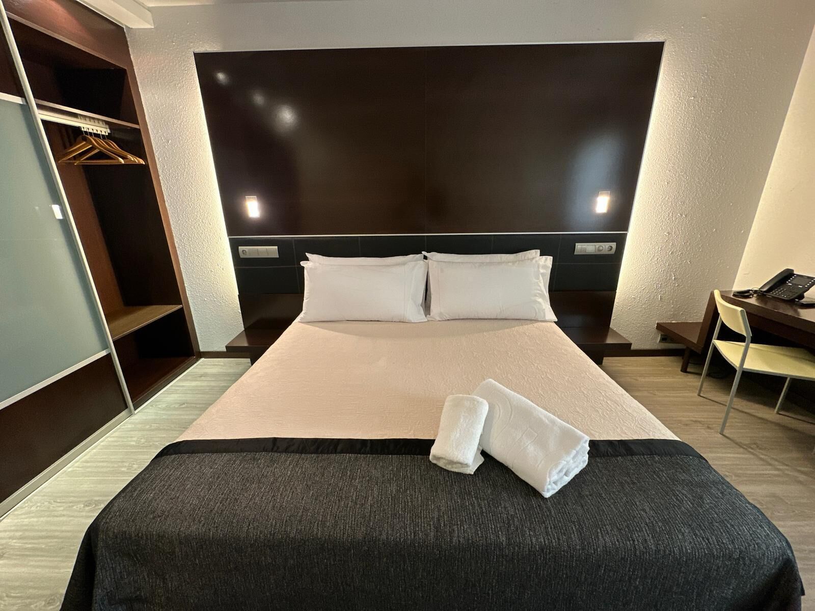 A hotel room with a bed, a desk, a chair, and a wardrobe.