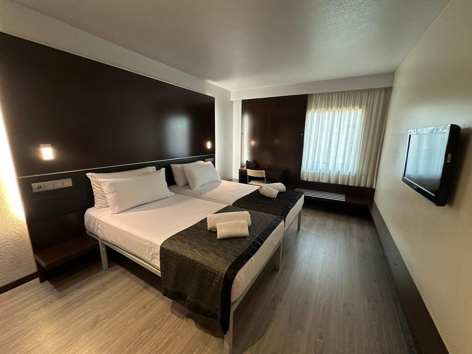 Una habitación de hotel con una cama, mesitas de noche, televisión y una ventana con cortinas.