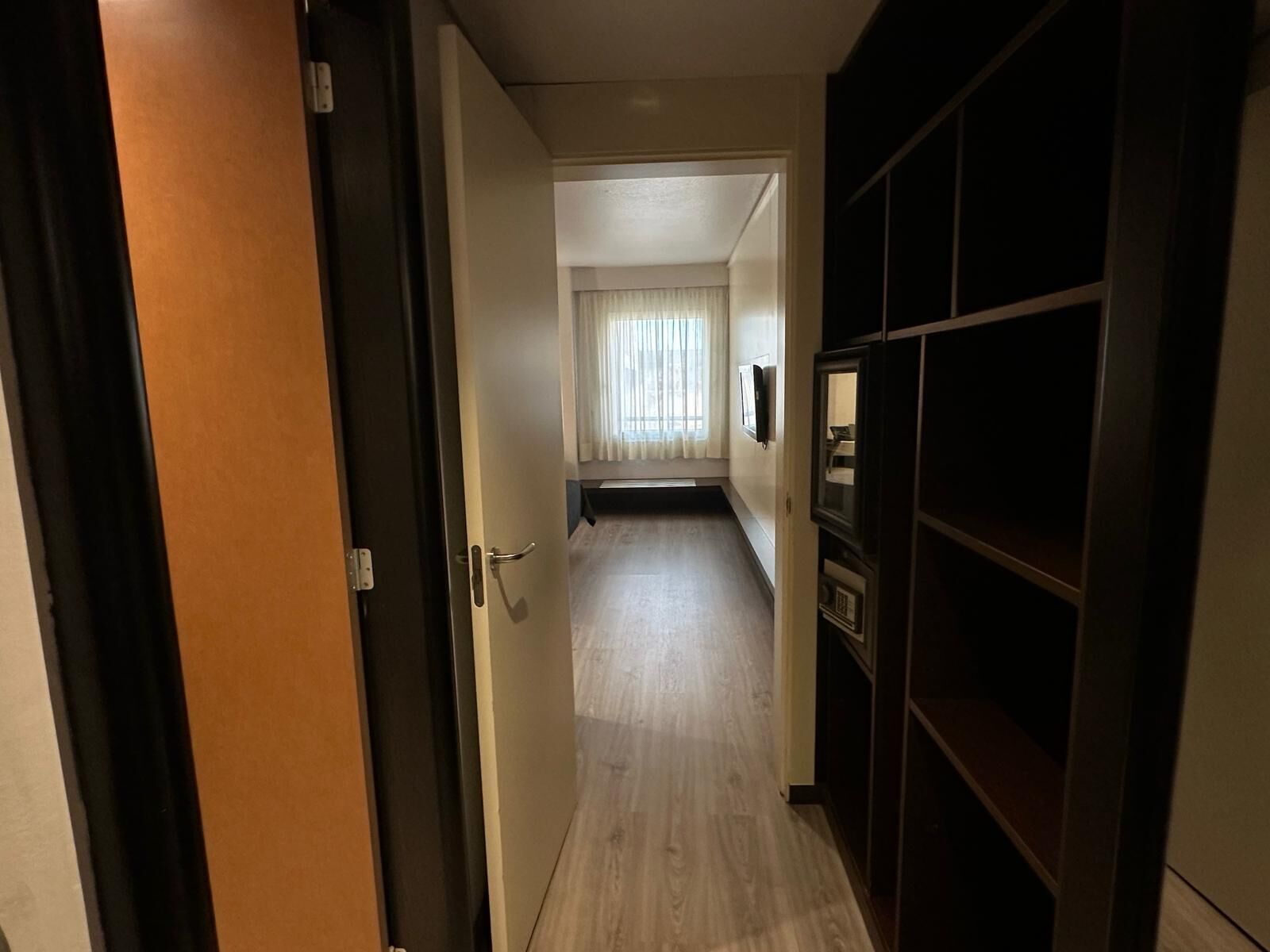 A hallway with a wooden door, a dark cabinet, and a window with curtains.