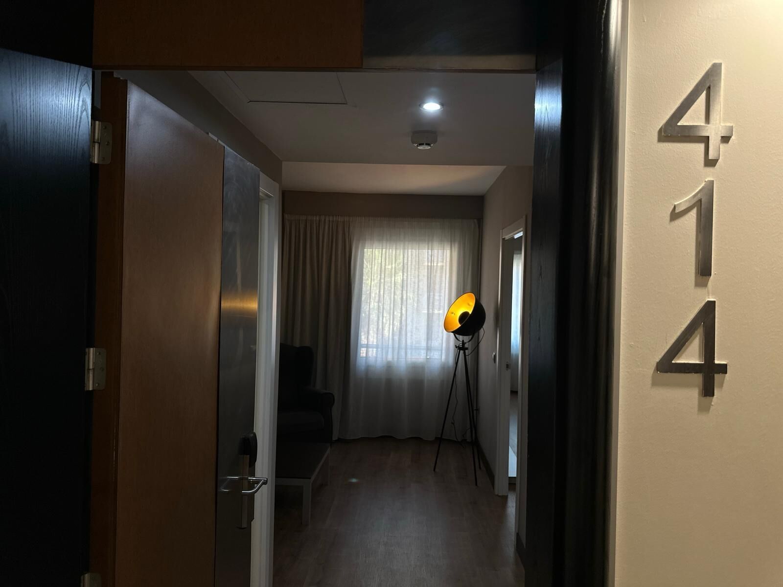 Un pasillo con una puerta a la izquierda, una lámpara a la derecha y el número 414 en la pared.
