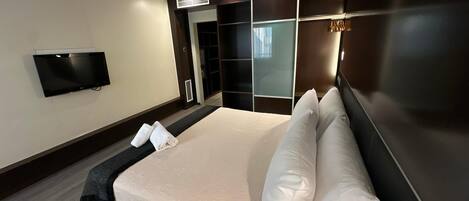 A modern hotel room with a large bed, a flat-screen TV, a walk-in closet, and a sliding glass door.