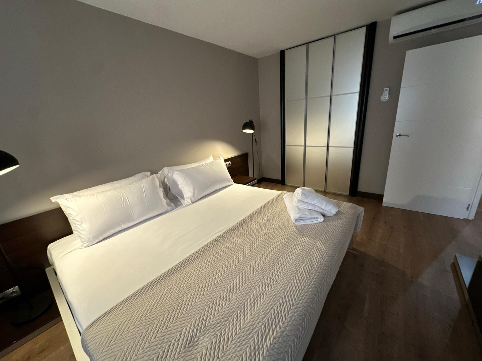 Une chambre d’hôtel avec un lit, une table de chevet, une lampe, une armoire et une porte.