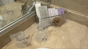 Kylpyhuone, jossa on lasinen suihkuseinä, lasinen pesuallas ja hygieniatuotteet läpinäkyvässä muovisessa säilytysastiassa.