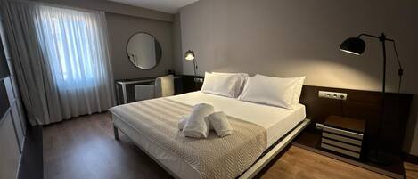 Una habitación de hotel con cama, lámpara de noche, escritorio, silla y espejo en la pared.