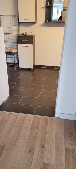 Eine Küche mit Fliesenboden, einem kleinen Schrank und einem Hocker.