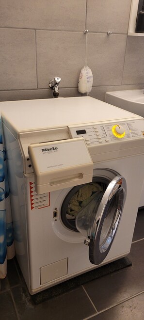 Eine Miele Waschmaschine mit Frontlader in einem Badezimmer mit gefliesten Wänden und einem Handtuchhalter.