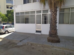 Ein Gebäude mit heller Fassade, vergitterten Fenstern, einer Palme und einem parkenden Auto.