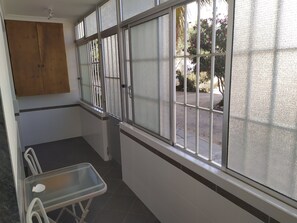 Ein Zimmer mit Fenster, Holzschrank, Glastisch und Stuhl.