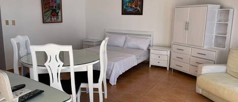 A bedroom with a bed, a small table with chairs, a cabinet, and two paintings on the wall.