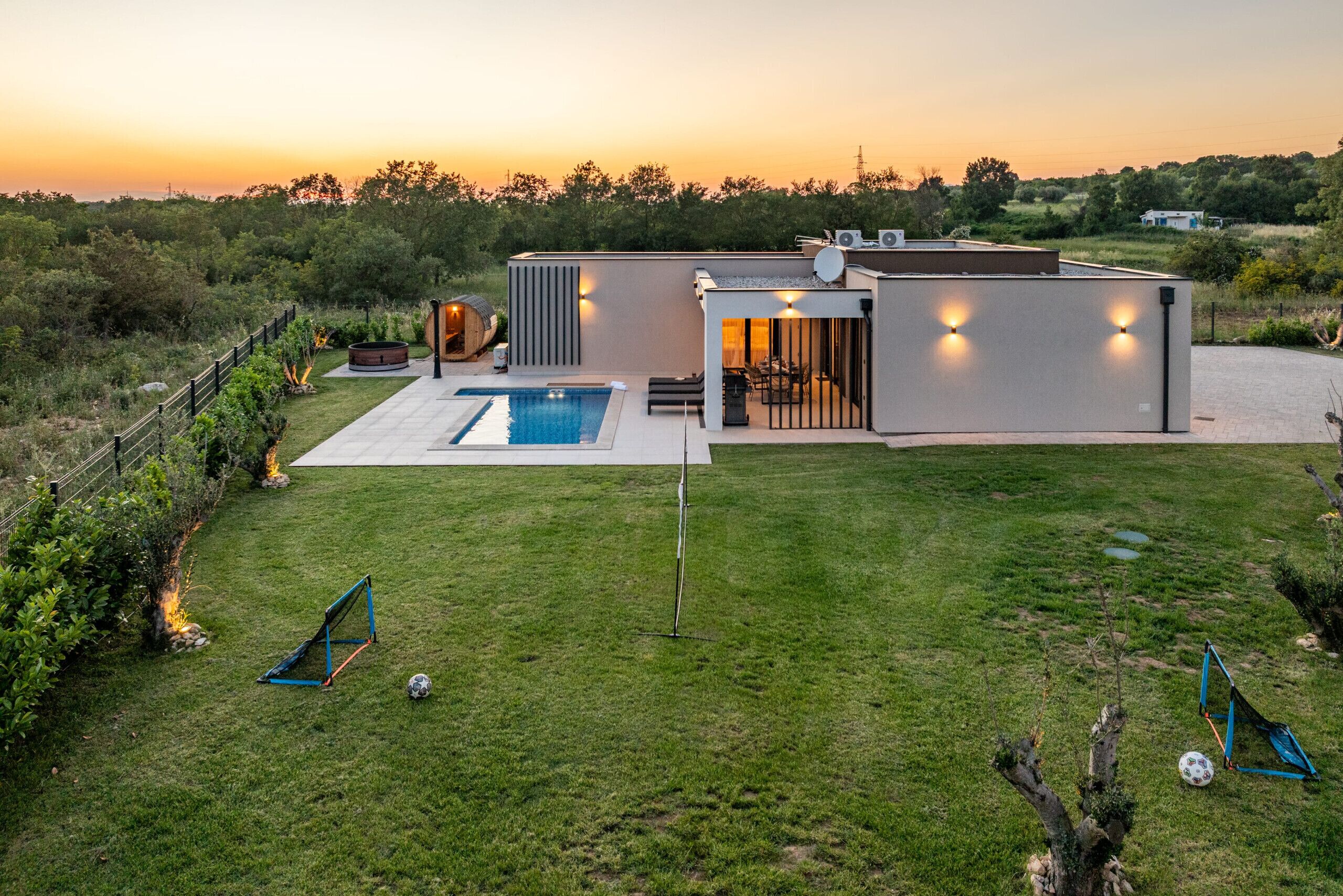 A modern house with a swimming pool, a patio, and a view of the sunset.
