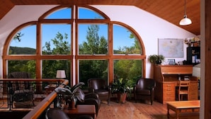 A spacious room with large arched windows, wooden flooring, and a desk with a chair. - Montagnard des Pays-d`en-Haut / Private Pool & Spa / Nature & Lake (Sainte-Adèle)