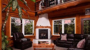 A cozy cabin interior with a fireplace, leather sofas, and large windows. - Montagnard des Pays-d`en-Haut / Private Pool & Spa / Nature & Lake (Sainte-Adèle)
