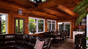 A wooden cabin interior with a leather sofa, dining table, chairs, and a bar area. - Montagnard des Pays-d`en-Haut / Private Pool & Spa / Nature & Lake (Sainte-Adèle)