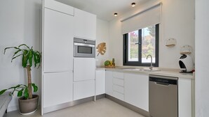 Una cocina moderna con armarios blancos, horno empotrado, lavavajillas y ventana con vista a follaje.