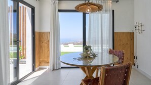 Un comedor moderno con una mesa de vidrio, sillas de madera, una lámpara colgante y vistas a través de un ventanal.