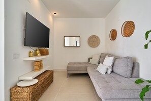 A living room with a flat-screen TV, a grey sofa, a small table, and decorative baskets. - Mediterranean Window: Rural House with Sea Views, Wi-Fi & Air Conditioning (Torrox)