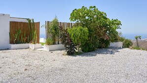Un espacio exterior moderno con suelo de grava, cerca de madera y diversas plantas, incluyendo un árbol grande.