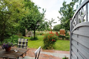 Un patio con mesa y sillas, rodeado de abundante follaje y un jardín.