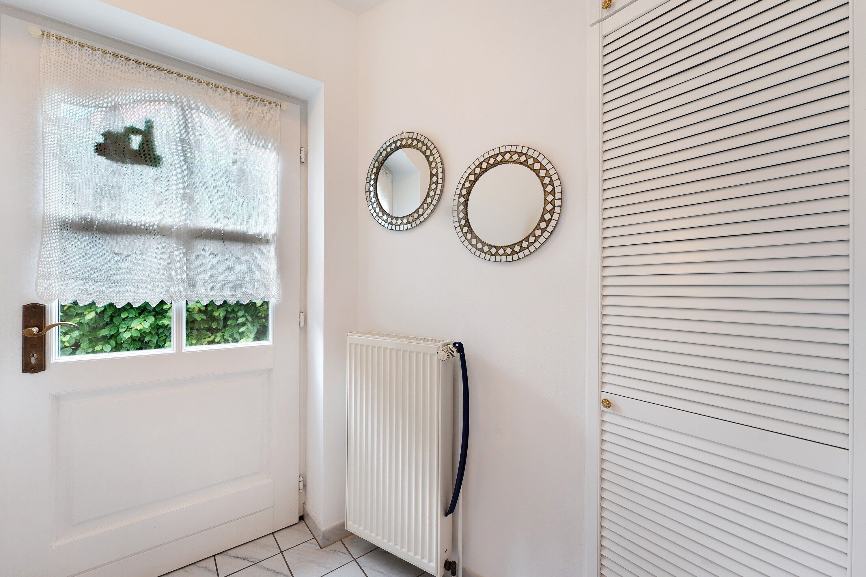 A white door with a window, a radiator, and two wall-mounted mirrors.