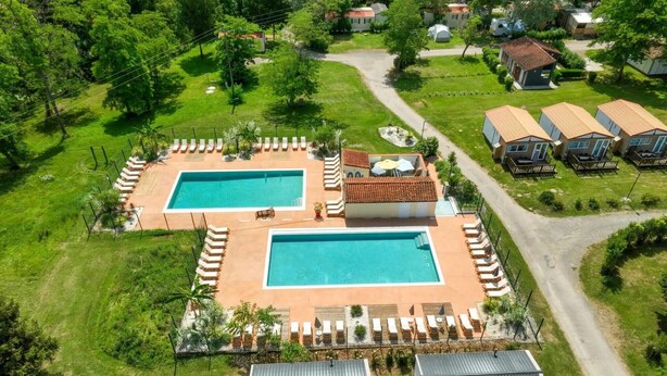 An aerial view of a resort with two rectangular swimming pools, a covered patio area, and several bungalow-style cabins.