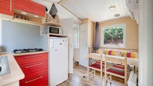 A compact kitchen with a refrigerator, microwave, and stove, a dining area with a bench, and a window with a view of greenery.