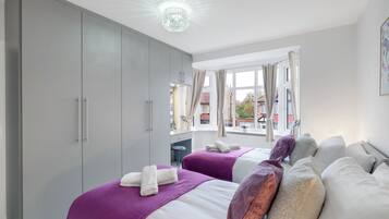 A hotel room with two beds, grey wardrobe, large window, and a chandelier.