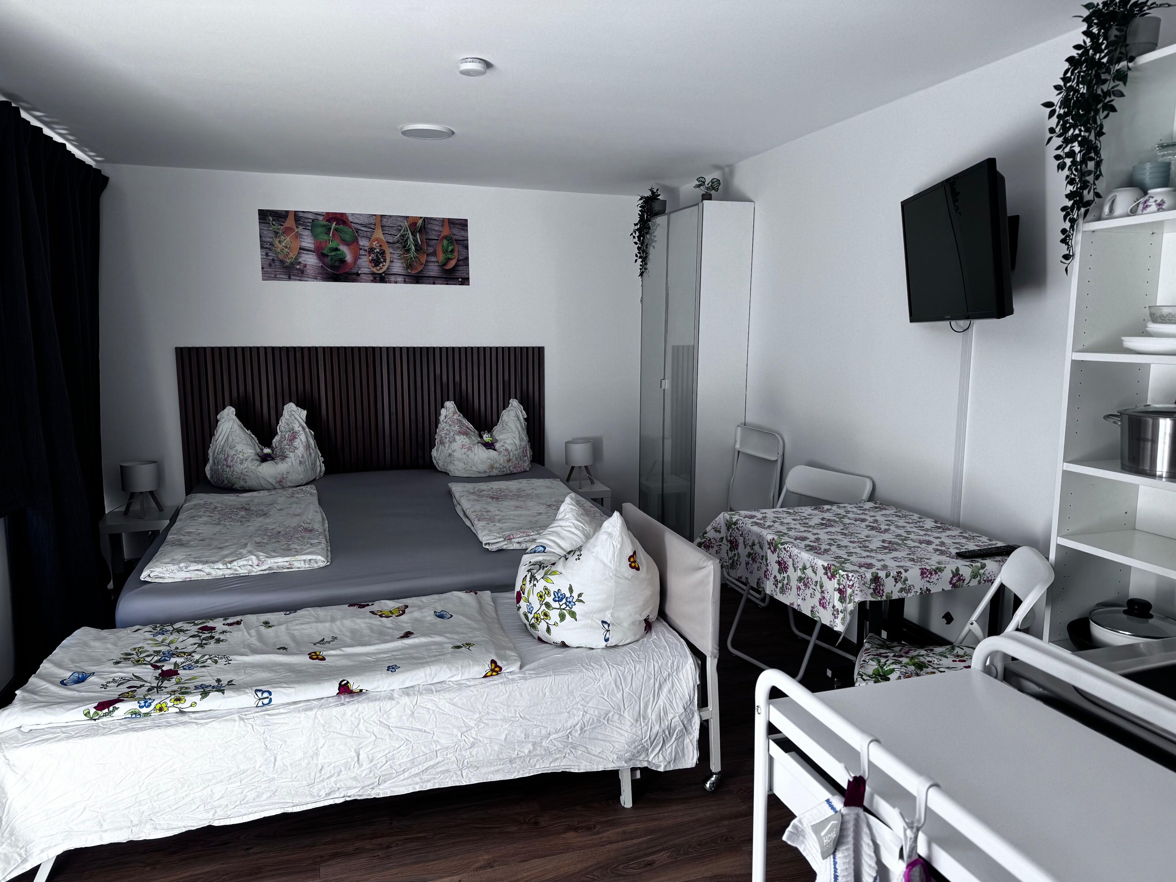 A hotel room with a bed, a bedside table, a TV, and a small table with a chair.