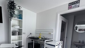 Una kitchenette compacta con pileta, microondas y estantes para almacenamiento.