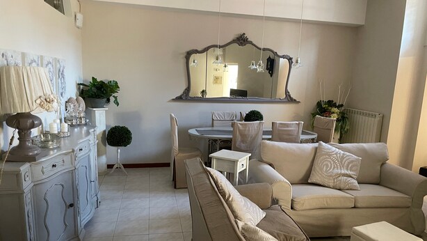 A living room with a sofa, a dining table, a cabinet, and a mirror. - Casa Mariuccia – 3 Bedrooms – In the Heart of Lucca (Lucca)