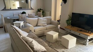 A living room with a sectional sofa, a TV stand, a dining table, and a large mirror. - Casa Mariuccia – 3 Bedrooms – In the Heart of Lucca (Lucca)