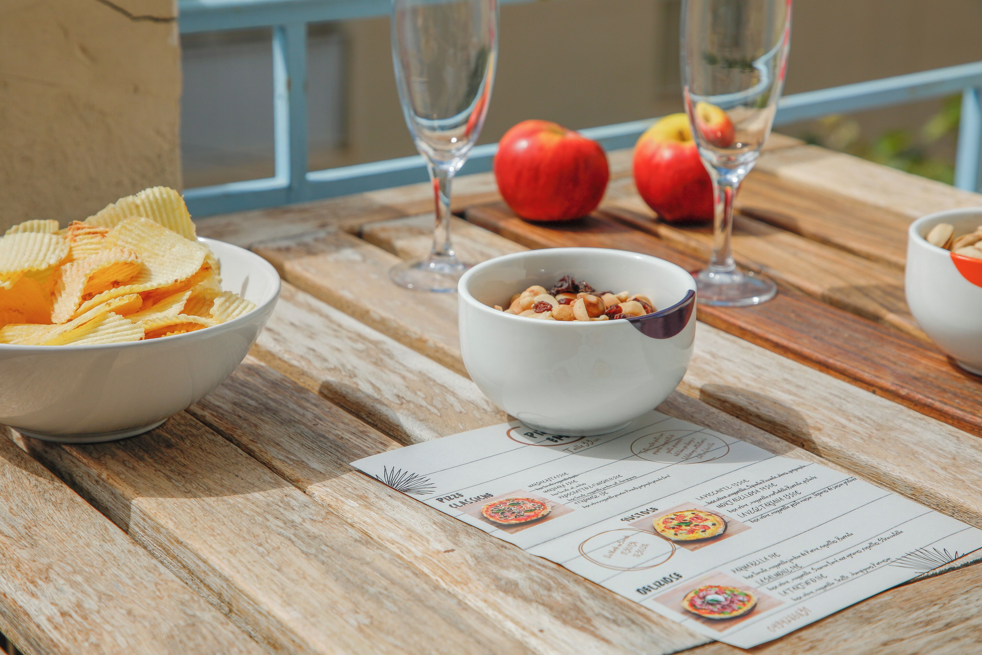 A wooden table with a bowl of snacks, two glasses of water, and apples.