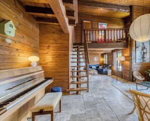 Ein Holzinnenraum mit einem Klavier, einer Treppe und einer Sitzecke mit Kissen.