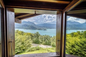 Ein schmiedeeisernes Fenster mit Blick auf einen See, Berge und Grünflächen.