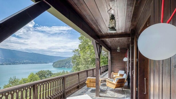 Un balcón de madera con muebles de mimbre con vistas a un lago y montañas.