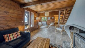 Un acogedor interior de cabaña con techo de madera, un sofá, una mesa de centro, una chimenea y una escalera que lleva a un nivel superior.