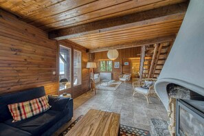 Ein gemütliches Blockhaus-Interieur mit Holzbalkendecke, einer Couch, einem Couchtisch, einem Kamin und einer Treppe zu einer oberen Ebene.