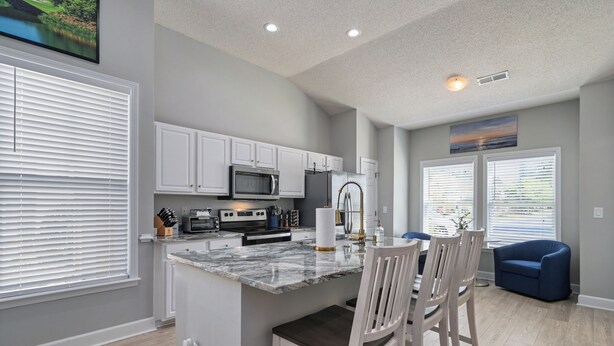 A modern kitchen with white cabinets, a marble island, and a dining area with a blue chair. - 3-B/R Townhome with Garage Murrells Inlet, The Clubhouse Retreat 
Near TPC (Murrells Inlet)