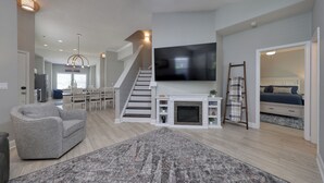A spacious living area with a fireplace, a flat-screen TV, a staircase, and a bedroom with a bed and dresser. - 3-B/R Townhome with Garage Murrells Inlet, The Clubhouse Retreat 
Near TPC (Murrells Inlet)