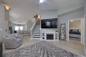 Ein großzügiger Wohnbereich mit Kamin, Flachbildfernseher, Treppe und einem Schlafzimmer mit Bett und Kommode.