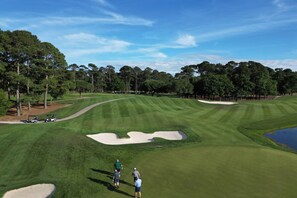 Ein Golfplatz mit Sandbunkern, Bäumen und blauem Himmel.