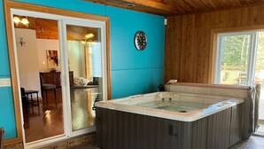 Un intérieur en bois avec un jacuzzi, une horloge et une vue sur l’extérieur.